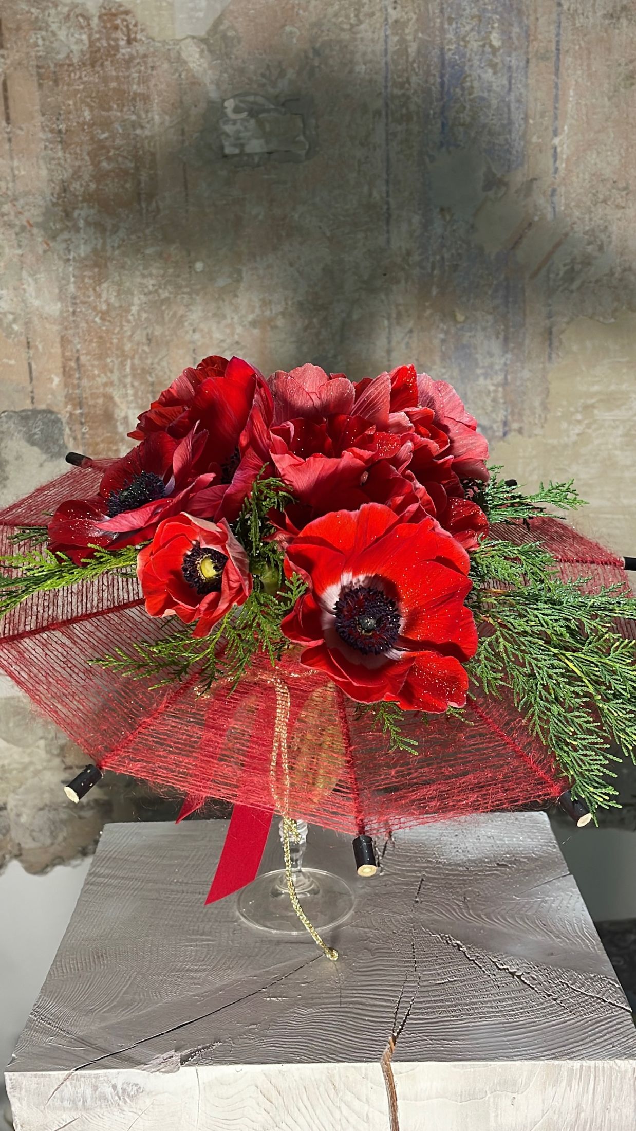 Bouquet di anemoni rossi avvolto in un velo rosso, su plinto davanti a una parete affrescata