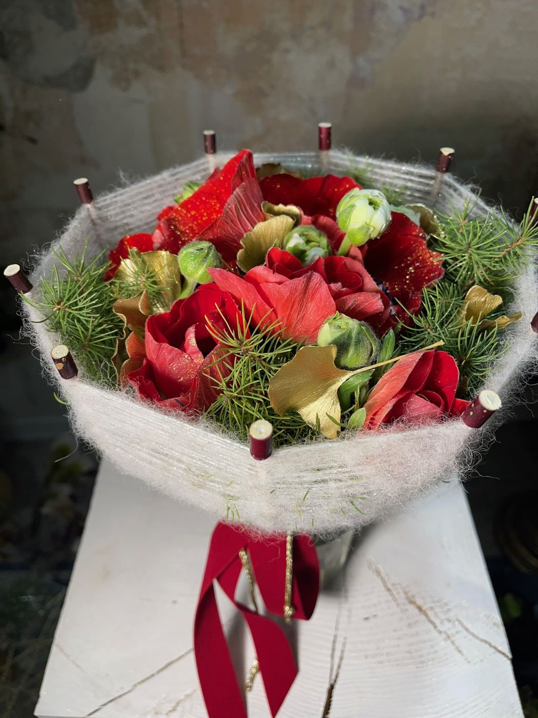 Bouquet di anemoni rossi avvolto in tessuto chiaro, su plinto